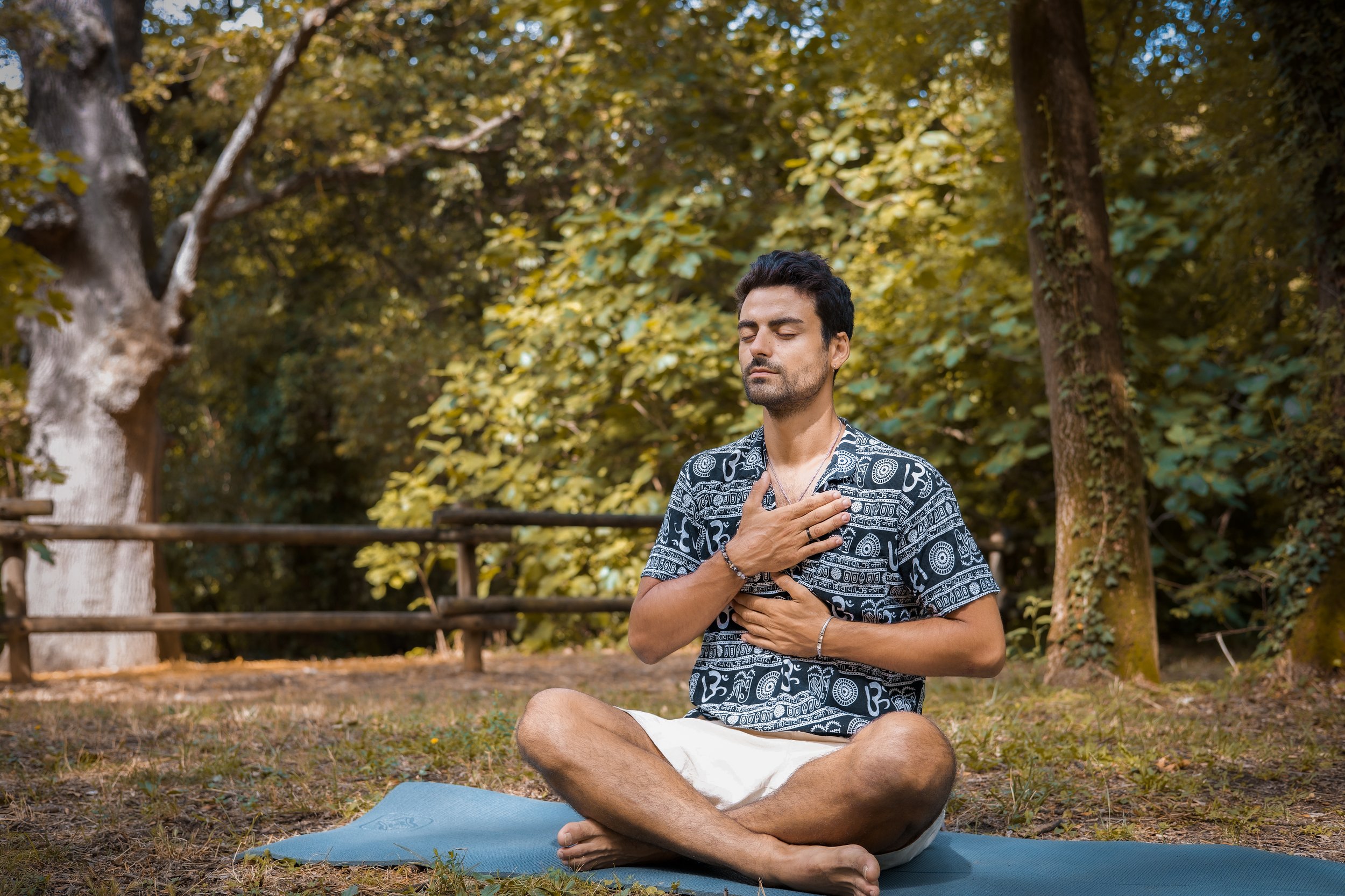 Homme méditant assis en tailleur sur un tapis dans un parc, la main sur la poitrine.